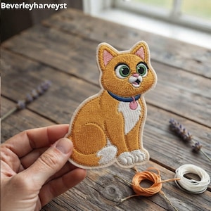 May include: An embroidered patch featuring an orange cat with large green eyes, a white chest, and white paws. The cat wears a blue collar with a small pink tag. The text 'Beverleyharveyst' is visible in the upper left corner of the image.