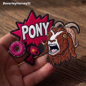 May include: Embroidered patches featuring a brown goat with an open mouth, a pink donut, a trophy, and a red burst with the word "PONY" in white. The patches have black borders and are likely for clothing or accessories.