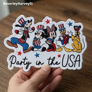 May include: Embroidered patch featuring Disney characters Goofy, Mickey, Minnie, Donald Duck, and Pluto in patriotic attire. The patch has the text "Party in the USA" and is outlined in white. Red, white, and blue colors are prominent.