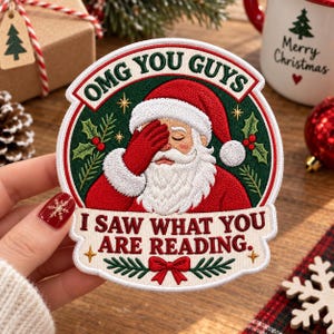 Puede incluir: Un parche bordado circular que muestra a Santa Claus con la mano en la cara en un gesto de decepción. El texto dice OMG YOU GUYS I SAW WHAT YOU ARE READING. El diseño incluye hojas de acebo verdes, bayas rojas y un lazo rojo sobre un fondo crema.