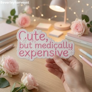 Op de afbeelding: Een witte, uitgestanste sticker met een geschulpte rand en de roze geborduurde tekst Cute, but medically expensive, geaccentueerd met kleine witte bloem- en sterpictogrammen. De sticker heeft een verhoogd, getextureerd uiterlijk met roze stiksels.