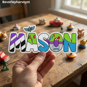 May include: A custom name sign spelling MASON in a colorful, stylized font inspired by space ranger aesthetics. The letters feature purple, white, black, green, and blue sections with a small wing graphic above the letter M. The text Beverleyharveyst is visible.