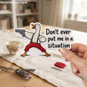 May include: An embroidered patch featuring a white goose wearing red pants and black suspenders, holding a grey handgun. The patch includes the black text 'Don't ever put me in a situation' in a bold, rounded font against a white background.