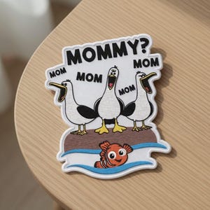 May include: Embroidered patch with three seagulls, open beaks, and the text "MOMMY?" and "MOM". An orange and white fish is below the seagulls. The patch has a white border.
