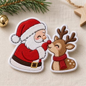 May include: An embroidered patch featuring Santa Claus in a red suit with a white-trimmed hat and a brown belt, touching the nose of a brown reindeer wearing a red scarf. The patch has a white border and detailed stitching throughout.