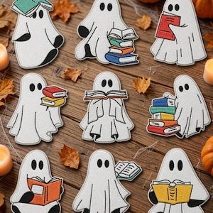 May include: Nine embroidered patches featuring white ghosts with black eyes and hands, each interacting with colorful books. The ghosts are shown in various poses, some holding stacks of books, others reading, or balancing books on their heads.