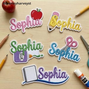 Puede incluir: Cinco parches bordados con el nombre Sophia en varios colores y diseños escolares, incluyendo una manzana roja, un lápiz amarillo, un frasco de pegamento morado, tijeras rosas y un cuaderno de espiral blanco sobre madera clara.
