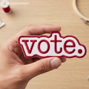 May include: A white embroidered patch with a red border and the word vote. in red lowercase letters. The patch has a scalloped, irregular shape that follows the contour of the text, featuring a clean, stitched finish on the edges.