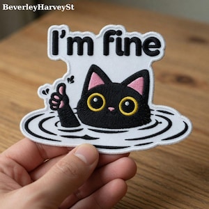 May include: Embroidered patch featuring a black cat with yellow eyes and pink ears, submerged in water. The patch has the text "I'm fine" in black letters on a white background. The cat is giving a thumbs up.