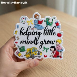 May include: White embroidered patch with the phrase "helping little minds grow" in black script. The patch features illustrations of a school bus, children, a teacher, a dragon, and school supplies.