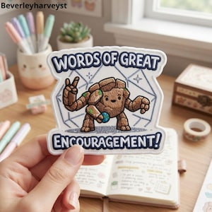 May include: A white embroidered patch with a dark blue border featuring a brown rock creature making a peace sign. The text reads WORDS OF GREAT ENCOURAGEMENT! in dark blue letters. The background of the patch shows a light blue geometric design.
