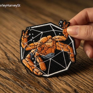May include: Embroidered patch featuring an orange figure within a black geometric design. The patch has a white border and is held against a wooden surface. The text "BeverleyHarveySt" is visible in the upper left corner.