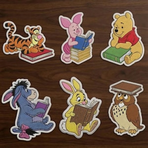 Puede incluir: Un conjunto de seis parches bordados con personajes de Winnie the Pooh leyendo libros. Tigger, Piglet, Pooh, Eeyore, Rabbit y Owl aparecen cada uno con un libro. Los parches tienen bordes blancos y un detallado trabajo de hilo colorido.