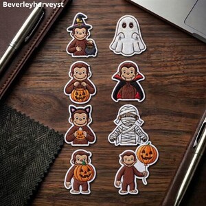 Peut inclure: Un ensemble de huit écussons brodés représentant un singe marron dans divers costumes d'Halloween, incluant un sorcier, un vampire, un chat et une momie, accompagnés d'un fantôme blanc et de plusieurs citrouilles d'Halloween orange.