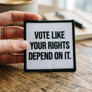 May include: A square fabric patch featuring a white background and a bold black border. The text VOTE LIKE YOUR RIGHTS DEPEND ON IT is printed in clear black capital letters in the centre of the patch, which has a clean and simple design.