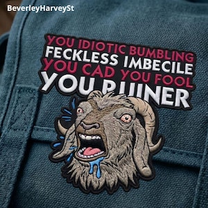 May include: Embroidered patch with a screaming goat design and the words "YOU IDIOTIC BUMBLING FECKLESS IMBECILE YOU CAD YOU FOOL YOU RUINER". The patch has a black background with white and red text, and is attached to a teal fabric.
