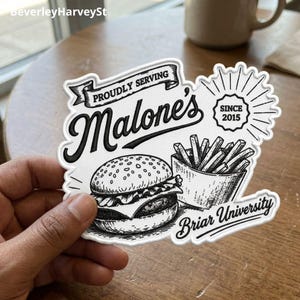 Könnte beinhalten: Schwarz-weißer Aufkleber mit einer Burger- und Pommes-Illustration und dem Text "PROUDLY SERVING Malone's SINCE 2015 Briar University". Der Aufkleber hat einen weißen Rand und wird von einer Hand gehalten.