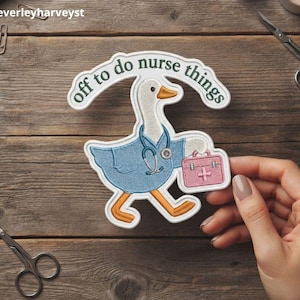 Puede incluir: Un parche bordado que muestra un ganso blanco con una casaca azul y un estetoscopio alrededor del cuello. El ganso lleva un botiquín médico rosa. Sobre el ganso, una pancarta arqueada contiene el texto en verde oscuro, off to do nurse things.