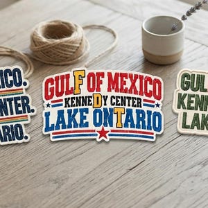May include: Three rectangular stickers featuring the text Gulf of Mexico, Kennedy Center, and Lake Ontario. The first sticker uses blue and red text with stars. The second uses red and blue text with a star. The third uses green and orange text.
