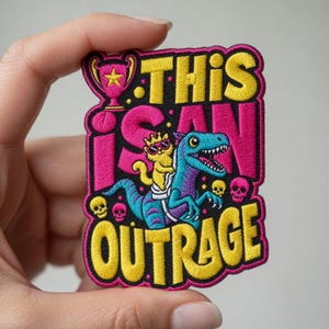 Peut inclure: Écusson brodé avec le texte "THIS I CAN OUTRAGE". L'écusson représente un chat de dessin animé portant des lunettes de soleil sur un dinosaure bleu et violet. Les couleurs rose, jaune et noir sont utilisées dans le design.