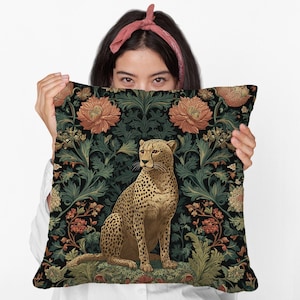 May include: Square throw pillow featuring a cheetah illustration. The cheetah is tan with black spots, set against a dark background with floral and foliage patterns in shades of green, orange, and brown.