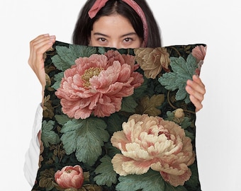 May include: A decorative pillow featuring a floral design with large, detailed peony blooms in shades of pink, peach, and cream. The pillow has a dark background with green leaves, creating a vintage aesthetic.