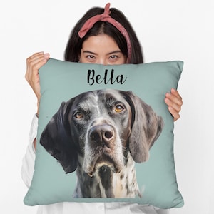 Pode incluir: Uma almofada quadrada azul clara com um retrato detalhado de um cão. O cão tem pelo preto e branco, olhos castanhos e orelhas longas e caídas. O nome "Bella" está escrito em script preto no topo.