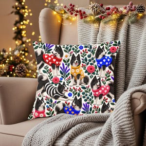 May include: A square throw pillow featuring a repeating pattern of black and white dogs wearing colorful sweaters with heart and flower motifs, interspersed with illustrations of red berries, blue flowers, and pink roses.