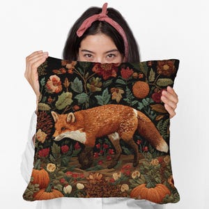 May include: A decorative pillow featuring a detailed illustration of a fox in a floral and foliage setting. The pillow has a black background with orange, red, and green accents. Pumpkins and flowers are also visible.