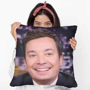 Puede incluir: Una almohada de tiro con una imagen impresa de un hombre con cabello castaño y una cara sonriente. La almohada es negra con un fondo blanco.