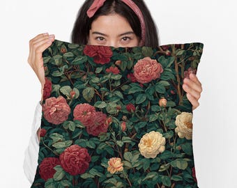 May include: A decorative square pillow featuring a floral pattern of red, pink, and yellow roses amidst green leaves. The pillow has a dark background and a vintage aesthetic, perfect for home decor.