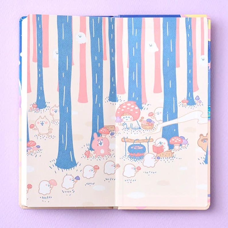 May include: An open notebook featuring a light pink background with blue tree trunks and a forest scene. The illustration includes small white ghost-like figures, a pink rabbit, and a character wearing a red mushroom cap near a cooking pot.