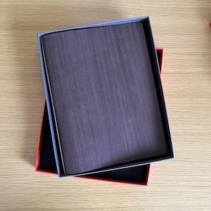 May include: A grey cardboard box with a red cardboard box inside. The grey box has a textured surface and the red box has a smooth surface.