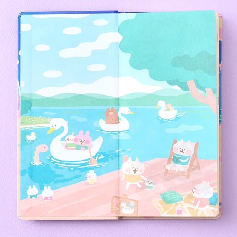 May include: An open notebook featuring a colorful illustration of a lake scene with cartoon animals. White swans float on blue water, while other characters relax on a pink shore under a large green tree. The sky is light blue with white clouds.