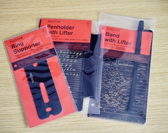 May include: Three black leather planner accessories in clear plastic packaging. The accessories are a ring supporter, a penholder with lifter, and a band with lifter. The packaging includes the product name and a description of the product.