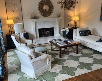 May include: A white and green geometric patterned rug in a living room with a white couch, a coffee table, and two white armchairs. The rug has a modern design with a geometric pattern of green and white.