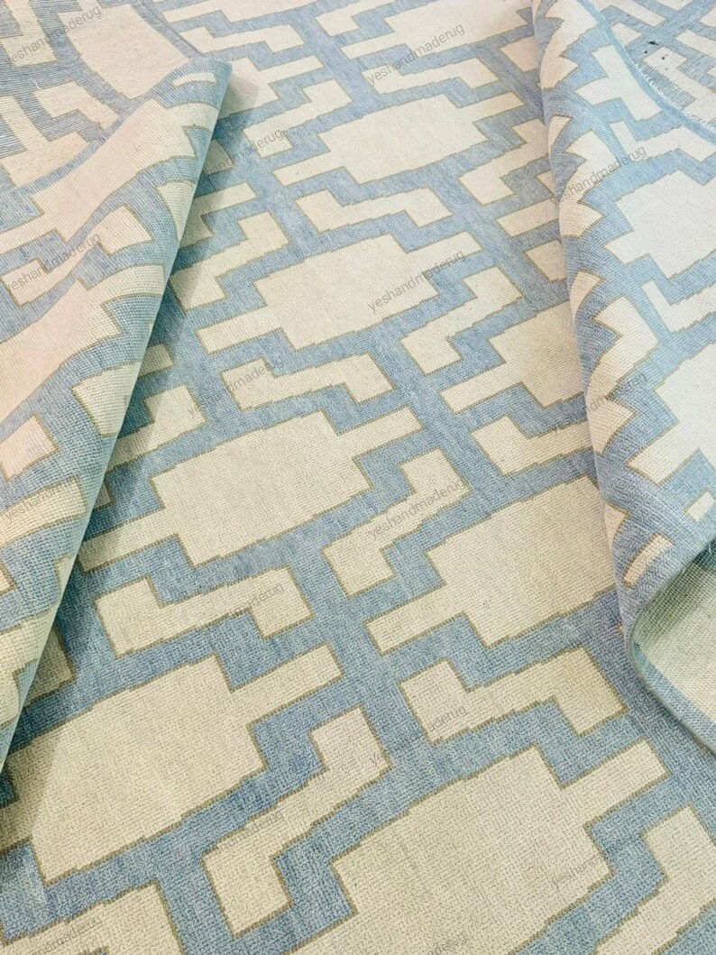 Top-down view of a modern handwoven rug highlighting its repeating geometric motifs and balanced color contrast. Crafted from premium wool, this flatweave area rug offers long-lasting quality and everyday comfort. The neutral beige base with soft blue accents suits minimalist and modern interiors. Ideal for living rooms, bedrooms, or open spaces, this handmade rug adds warmth, texture, and contemporary style
