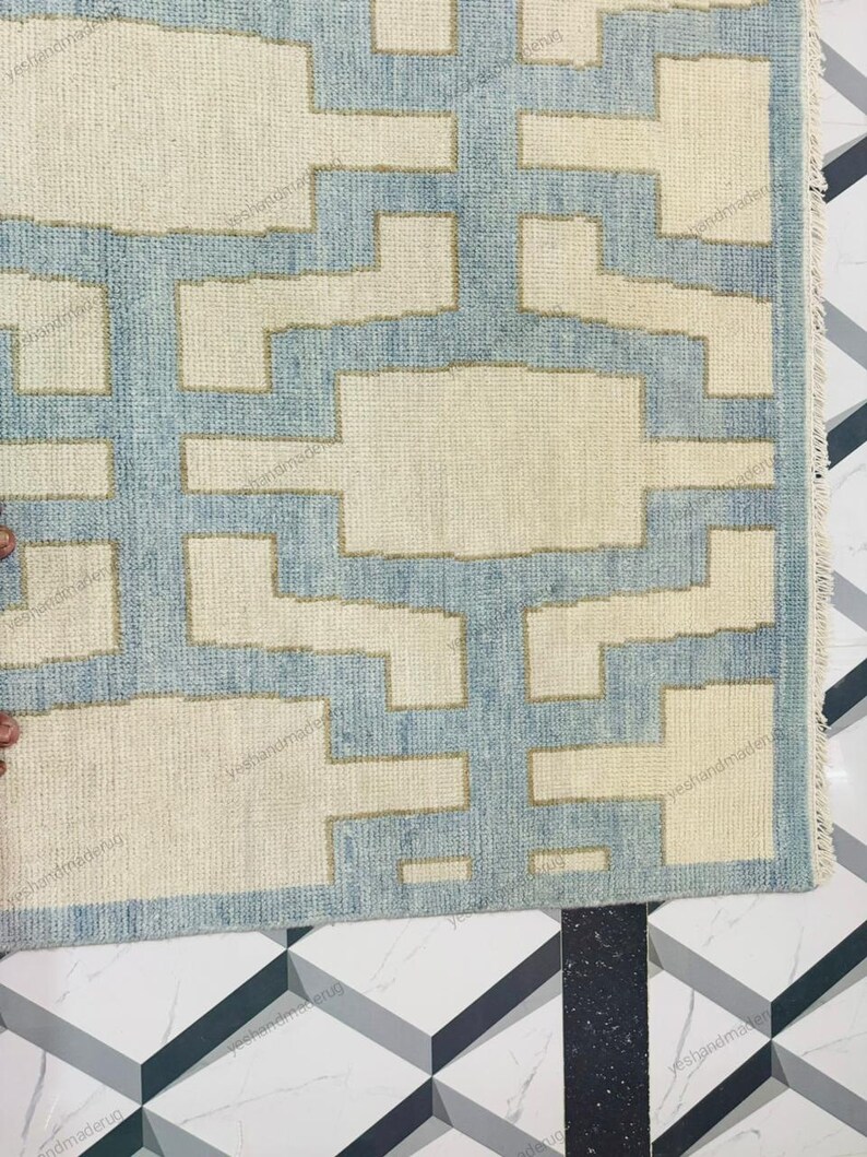 Elegant handwoven wool rug photographed from a corner angle to display its precise geometric pattern and neat edges. This modern flatweave rug features a minimalist abstract design in neutral beige with soft blue accents. Ideal as a living room rug or bedroom rug, it complements modern, bohemian, and coastal décor styles. Crafted by skilled artisans, this handmade area rug offers durability, style, and timeless appeal for contemporary homes.
