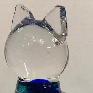 Könnte beinhalten: Eine blaue und grüne Glaskatzenfigur mit einem klaren Glaskopf und -ohren. Die Figur hat einen runden Aufkleber an der Seite mit der Aufschrift "Murano & C."