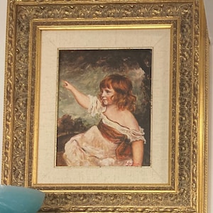 May include: A framed oil painting of a young girl in a white dress with a brown sash, standing in a forest setting. The painting is in a gold frame with ornate details.