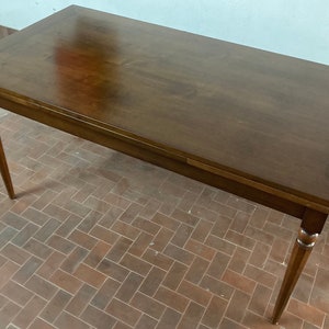 May include: A dark brown wooden extendable dining table with a smooth, polished surface. The table has four legs with turned details and a rectangular top.