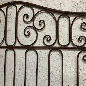 Può includere: Un cancello in metallo arrugginito con un designo decorativo di volute e curve. Il cancello è in ferro battuto e ha uno stile tradizionale.