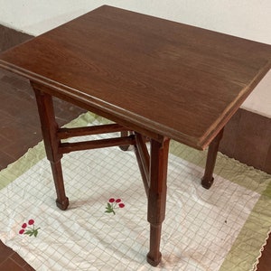 May include: A dark brown wooden table with a rectangular top and a unique, geometrically designed base. The table is sitting on a white and green checkered tablecloth.