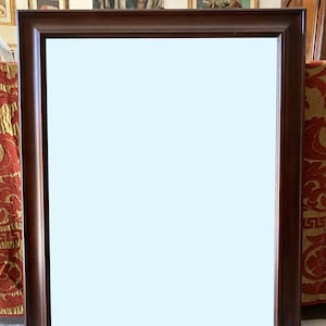 May include: A dark brown wooden mirror with a shelf underneath. The mirror has a simple frame and a plain white reflection.