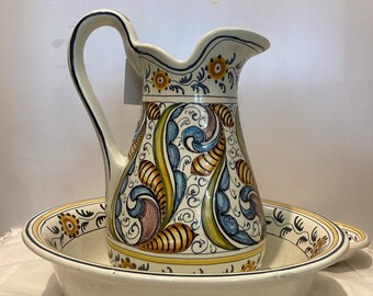 Op de afbeelding: Een witte keramische kan met een blauw, geel en bruin bloemenmotief. De kan staat in een witte keramische kom met een blauw en geel bloemenmotief.