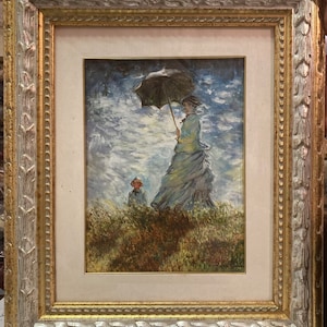 May include: A framed painting depicting a woman in a blue dress holding an umbrella, walking with a child in a field. The painting is set against a cloudy sky.