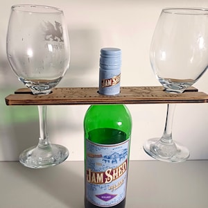 Könnte beinhalten: Holz-Wein- und Glashalter mit dem Text "Wahre Liebe hält wie Wein, sie wird mit dem Alter stärker". Der Halter hat zwei Fächer für Weingläser und Platz für eine Flasche. Eine Flasche Jam Shed Malbec Wein befindet sich im Halter.