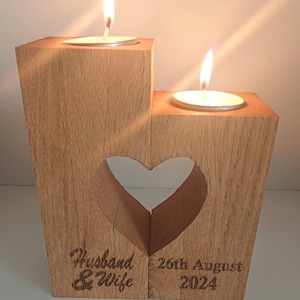 May include: Wooden candle holder with a heart-shaped cutout. The holder has two candle wells and is engraved with "Husband & Wife" and "26th August 2024".