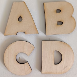 May include: Four wooden letters, A, B, C, and D, are arranged in a square shape. The letters are cut out of a light brown wood and have a slightly distressed look.