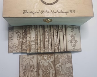 May include: A wooden box with a light blue interior, containing a full deck of Rider-Waite tarot cards. The box lid features an eye symbol and the text "The original Rider-Waite design 1909". The cards are arranged in a stack, with the Justice, Devil, and Temperance cards visible at the bottom.